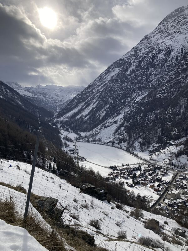 Blick in das verschneite Dorf im Tal und der Sonne, welche durch die Wolken scheint